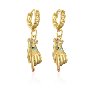 Detail of gold-plated hand charms earrings with blue evil eye and red nails on white background