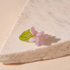 Close-up of beaded flower ring with lilac petals and green band on marble stone