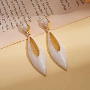 Detailed view of vintage gold water-drop earrings with white enamel on a book page