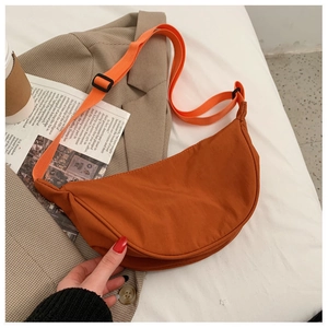 Adjustable orange nylon crescent bag on a brown blazer with a stylish lifestyle background