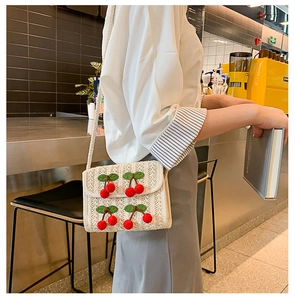 Detailed view of cream straw shoulder bag with cute red 3D cherry accents and weave strap