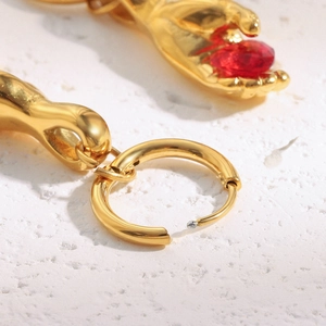 Macro detail of 18K gold plated earring featuring a hand holding a red gemstone