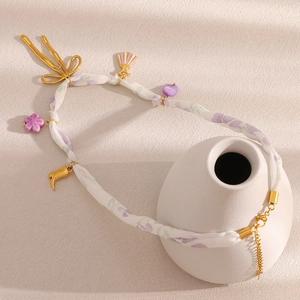Detail der floralen Bandkette mit goldenen Anhängern an einer weißen Keramikvase