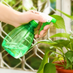 Green translucent garden spray bottle for watering plants in a sunny outdoor setting
