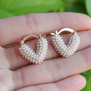 Elegant gold heart-shaped earrings with micro pearl inlays held in palm for scale