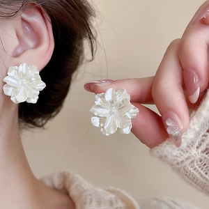 Macro view of creamy white camellia flower stud earring worn by model with pearl details