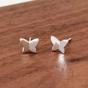 Macro view of S925 sterling silver butterfly stud earrings on textured wood
