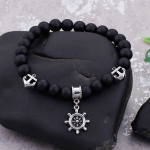 Macro detail of nautical beaded bracelet featuring anchor and helm charms on rock surface