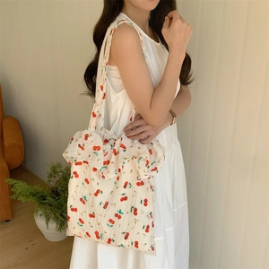 Detail of canvas tote bag with red cherry prints and ruffle trim styled with a white dress