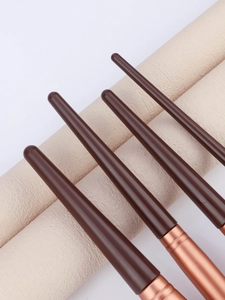 Detail of chocolate brown tapered handles and polished rose gold ferrules on makeup brushes