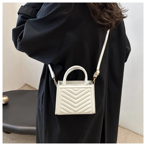White quilted shoulder bag with V-shaped stitching and gold hardware shown on model