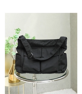 Detail of a black canvas messenger bag with double front pockets on a metal table