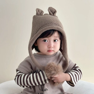 Detail of baby winter knit hat with pom-pom ears and warm earflaps in brown color