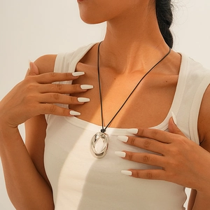 Detail of a silver irregular hollow pendant on a black cord necklace worn by a model