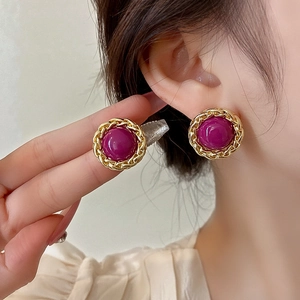 Close-up of vintage gold twisted metal earrings with round burgundy gemstone on a model