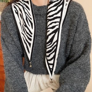 Close-up of zebra stripe knit scarf with golden bell charm on grey knit sweater