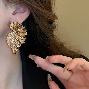 Golden metal leaf earrings with realistic vein texture on professional female model
