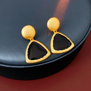 Detail of vintage gold earrings with textured metal and black geometric enamel inlay