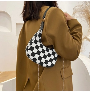 Model wearing a black and white checkerboard baguette bag with a gold chain strap