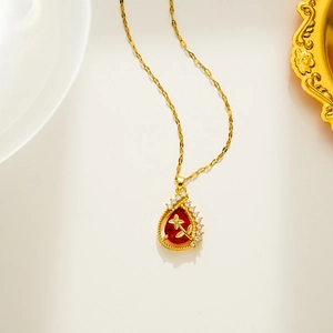 Golden necklace with red water drop pendant and micro-set cubic zirconia on white surface
