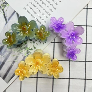 Detailed top view of three gradient plumeria hair claws in teal, purple, and yellow finish