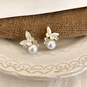 Macro view of gold butterfly pearl earrings with sparkling crystals on textured porcelain