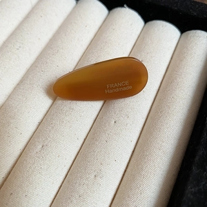 Détail de la barrette goutte en acrylique ambre avec texte France Handmade sur velours beige