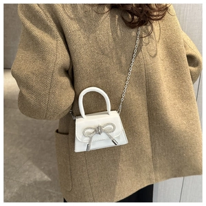 Detail of white mini crossbody bag with a rhinestone bow and silver chain strap