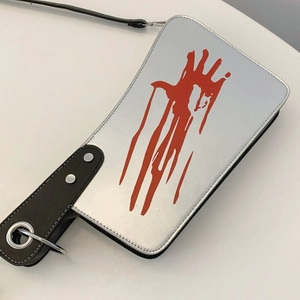 Macro shot of silver cleaver bag with red blood handprint and metallic rivet detail