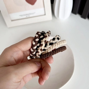 Close-up of five woven lily-of-the-valley hair ties in assorted neutral earth tones