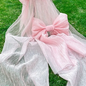 Pink pleated silk bow for outdoor wedding chairs and event decor on a green lawn