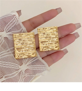 Detailed view of gold rectangle stud earrings with a textured hammered metal finish