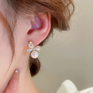 Close-up of model wearing gold bow earrings with zircon accents and dangling round pearls