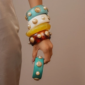 Macro detail of wide resin bangles with marble textures, seashells, and pearls