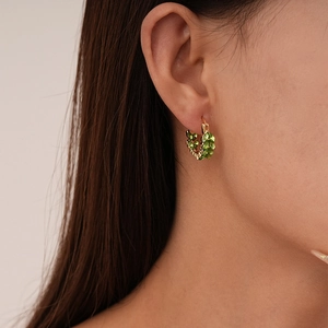 Close-up of gold wheat ear U-shaped hoops with green crystals on a model's ear