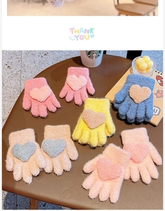 Close-up of knit children's gloves featuring colorful plush heart patches for winter