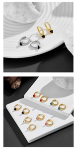 Detail of colorful heart charm hoop earrings with crystal settings on white display pedestal