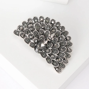 Macro shot of silver-gray peacock brooch with black crystals on a white pedestal