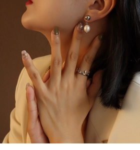 Detail shot of elegant silver pearl drop earrings and a sculptural silver ring on a model
