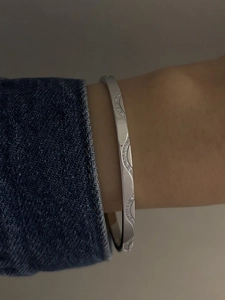 Close-up of a silver wavy stainless steel bangle with zircon inlay on a woman's wrist