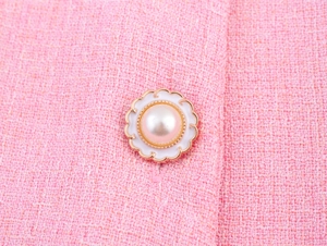 Nahaufnahme eines Perlen-Blumenknopfes auf einem rosa Tweed-Stoff für Damenmode