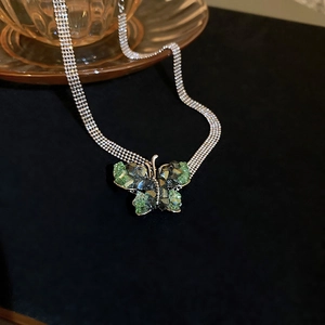 Macro detail of a green crystal butterfly pendant on a silver multi-row chain necklace