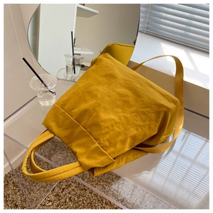 Close-up of mustard yellow pleated nylon bag with dual handles and soft texture
