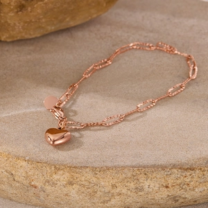 Detail of rose gold paperclip chain bracelet with polished heart pendant on warm stone