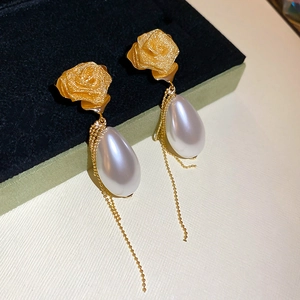 Detail of gold rose earring with drop pearl and delicate metal tassels in jewelry box