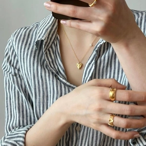 Close-up of golden heart pendant necklace with pearl and matching gold rings on model