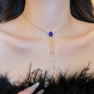 Detail of gold Y-necklace with blue rectangular pendant and delicate sparkling tassels