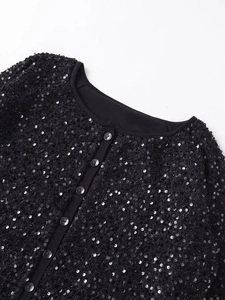 Dettaglio ravvicinato di paillettes nere e bottoni su una giacca con scollo rotondo