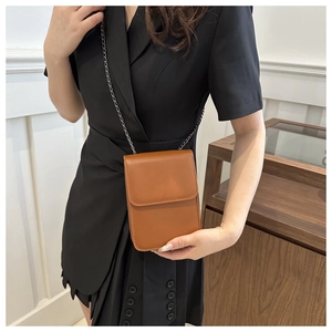 Brown leather crossbody phone bag with metal chain strap worn by a model in black