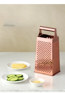 Macro view of rose gold box grater with diverse blades and cucumber slices on countertop